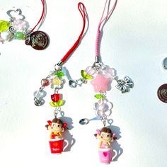 three charms are hanging on a white surface, one is pink and the other is green