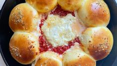 a pan filled with bread rolls covered in cheese and marinara sauce, on top of a white table