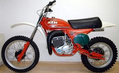 an orange and black dirt bike parked next to a white wall