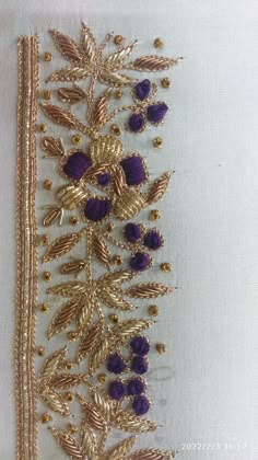 a gold and purple beaded trim with leaves on the side, attached to a white fabric