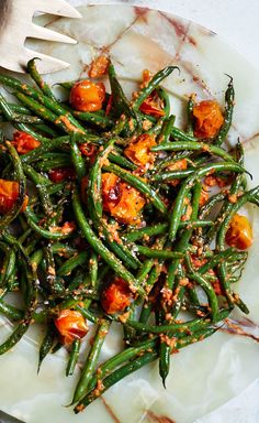 a white plate topped with green beans covered in toppings and a fork next to it