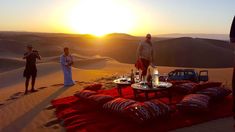 two people standing on top of a sand dune next to a table with food and drinks