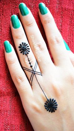 a woman's hand with green fingernails and tattoos on her fingers, holding a black flower