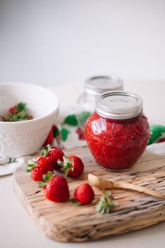 some strawberries are sitting on a cutting board next to a bowl and spoons