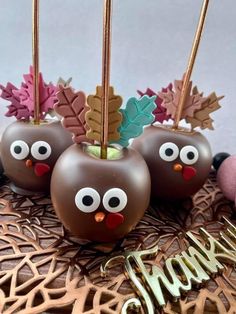 three chocolate apples decorated like turkeys with leaves and acorns on top are sitting on a table