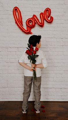 a young boy holding flowers in front of a love sign