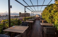 an outdoor dining area with wooden tables and chairs overlooking the cityscape at sunset