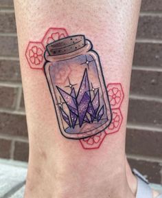 a tattoo on the leg of a woman with a glass jar filled with purple crystals