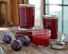 three jars filled with jam sitting on top of a wooden table next to plums