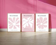 three pink posters with white flowers on them in front of a pink wall and wooden floor