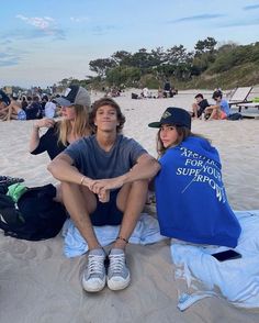 a man and woman sitting on the beach next to each other