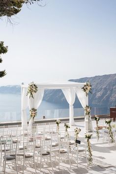 an outdoor wedding setup with white drapes and floral arrangements on the side of the aisle