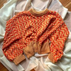 an orange and yellow sweater sitting on top of a white sheet