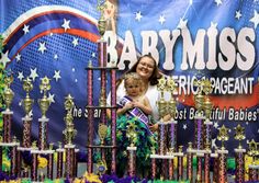 a woman holding a small child in front of trophies