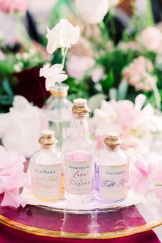 three bottles of perfume sitting on top of a table next to pink and white flowers