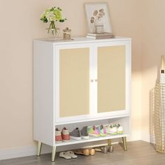 a white cabinet with shoes on the bottom shelf and flowers in vase next to it