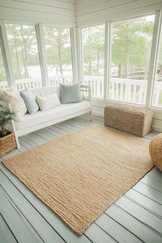 a porch with white furniture and large rugs on the wooden floor, along with two wicker baskets