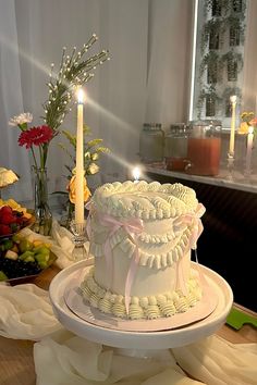 a white cake sitting on top of a table next to candles and flowers in vases