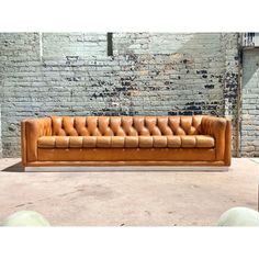 a tan leather couch sitting in front of a brick wall