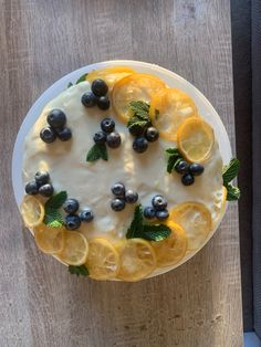 a cake with lemons, blueberries and mint leaves on it sitting on a table