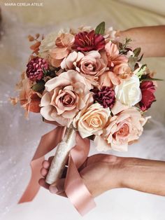 the brides bouquet is being held in her hands with pink ribbons around it and she also has an orange rose