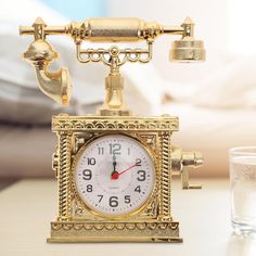 a golden clock sitting on top of a white table next to a glass of water