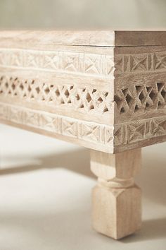 a wooden bench with intricate carvings on the top and bottom, sitting on a white surface