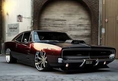 a black and red muscle car parked in front of a garage door with brick floors