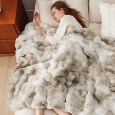 a woman laying in bed covered with a fluffy blanket