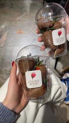 two people holding up some strawberries in plastic containers with stickers on the top