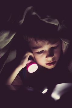 a young boy laying in bed while talking on a cell phone with his head turned to the side