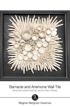 an art piece with white shells and black frame on the wall above it is text that reads, barnacle and anemone wall tile hand - built ceramic