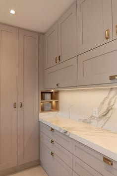 a kitchen with white cabinets and marble counter tops on both sides, along with gold pulls