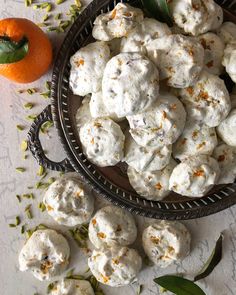 a bowl full of white cookies next to an orange and some leaves on the table