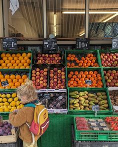 a woman standing in front of a fruit stand with oranges, apples and other fruits