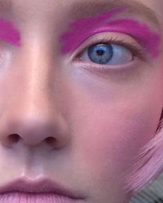 a woman with pink hair and blue eyes has bright pink makeup on her face, while she is looking at the camera