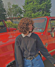 a woman standing in front of a red truck with her hand on the door handle