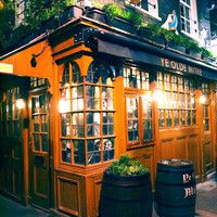 the outside of a pub at night with lights on and plants growing out of it