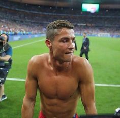 a shirtless man standing on top of a soccer field next to a cameraman