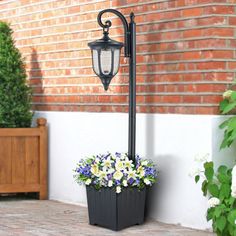 a lamp post with flowers in it next to a brick wall and potted planter