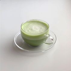 a glass cup filled with green liquid sitting on top of a saucer