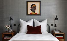 a bed with white linens and red pillows in a gray room next to a painting on the wall