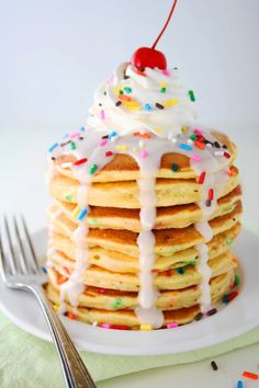 a stack of pancakes covered in icing and sprinkles with a cherry on top