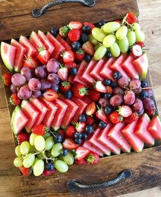 a wooden cutting board topped with watermelon, grapes and strawberries