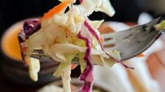 a close up of a fork with food on it and a bowl in the background