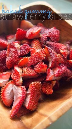 sliced strawberries in a wooden bowl on top of a cutting board with the words baked gummy strawberries slices