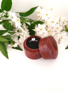 a wooden ring box sitting next to some white flowers and green leaves on a white surface