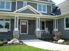 a gray house with two white rocking chairs on the front porch and large stone steps leading up to it