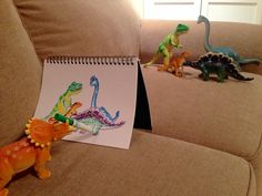 three toy dinosaurs sitting on a couch next to a notepad with the word dino