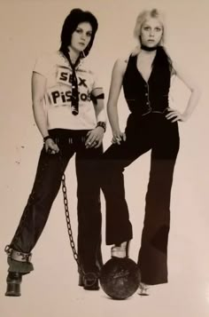 two women standing next to each other in front of a wall with chains on it